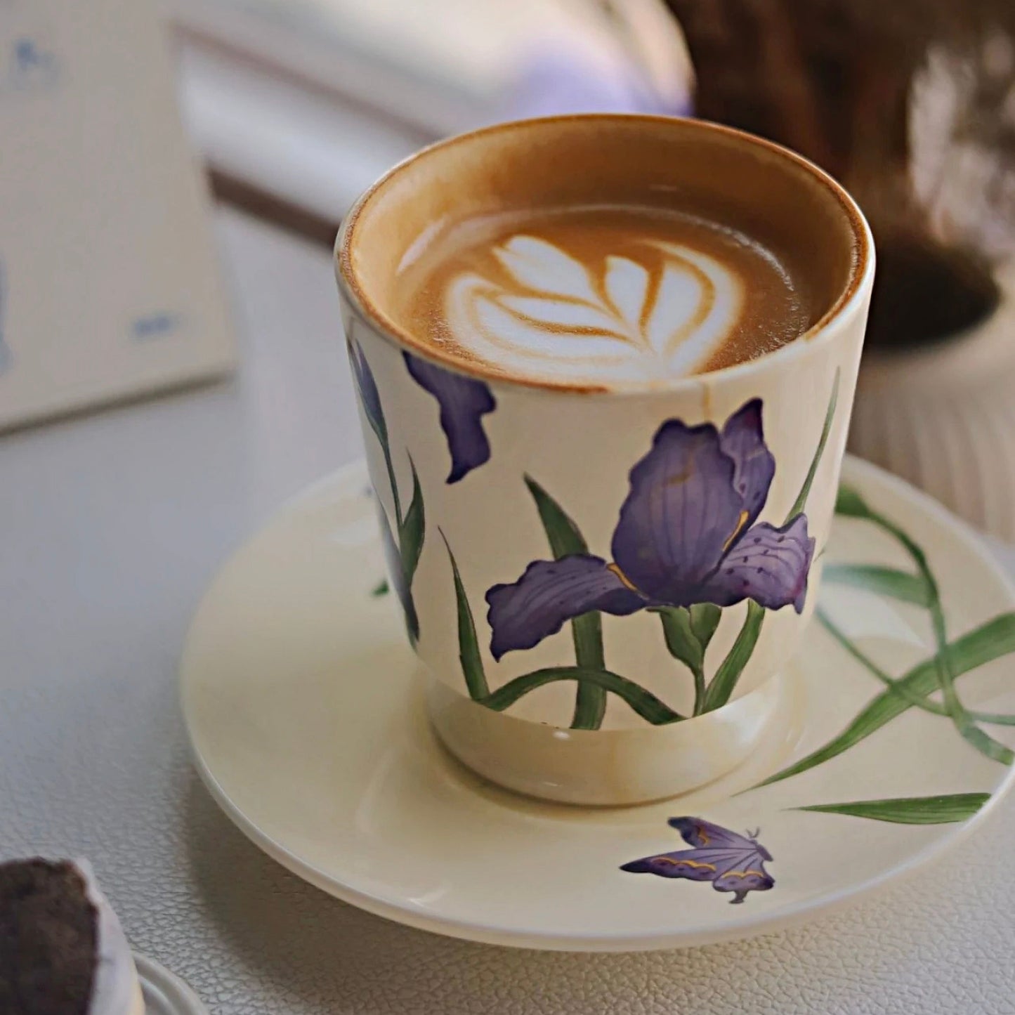 A handcrafted ceramic coffee mug featuring a delicate purple iris floral design, paired with a matching saucer for an elegant tea or coffee experience.