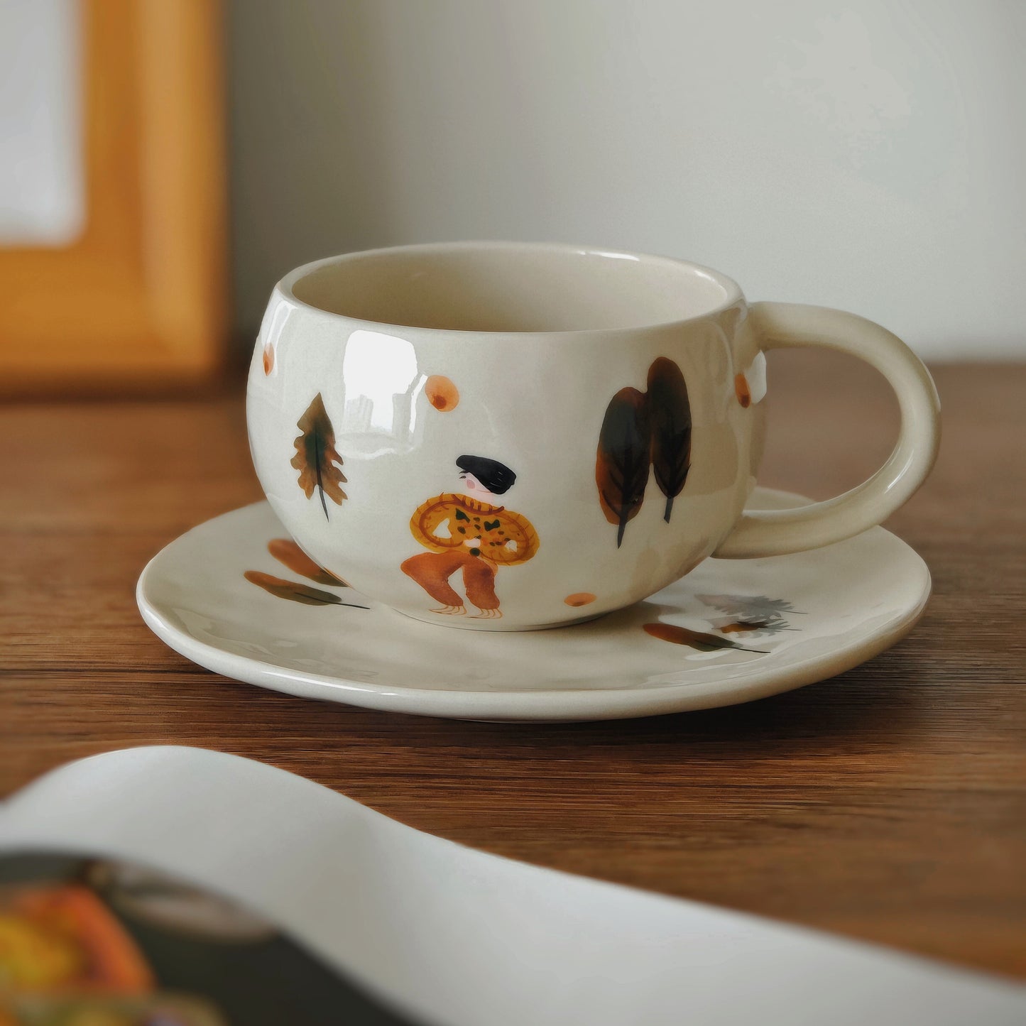 Close-up of an artisan-style coffee cup and saucer set showcasing delicate foliage, a little girl in a leaf cape, and soft beige glaze. This artistic ceramic cup set is both microwave-safe and dishwasher-safe, perfect for cozy tea rituals, gift ideas for coffee lovers, and stylish home essentials.