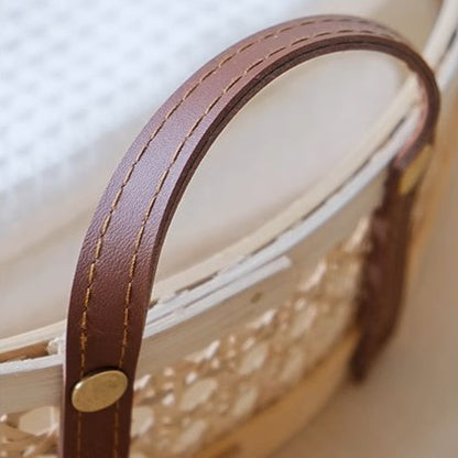 Close-up of the sturdy leather handles on a round rattan wicker storage tray, showcasing the craftsmanship and attention to detail.