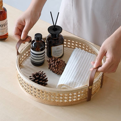 Round rattan wicker storage tray with leather handles, holding candles and decorative items in a living room, available in natural and walnut wood colors and multiple sizes.