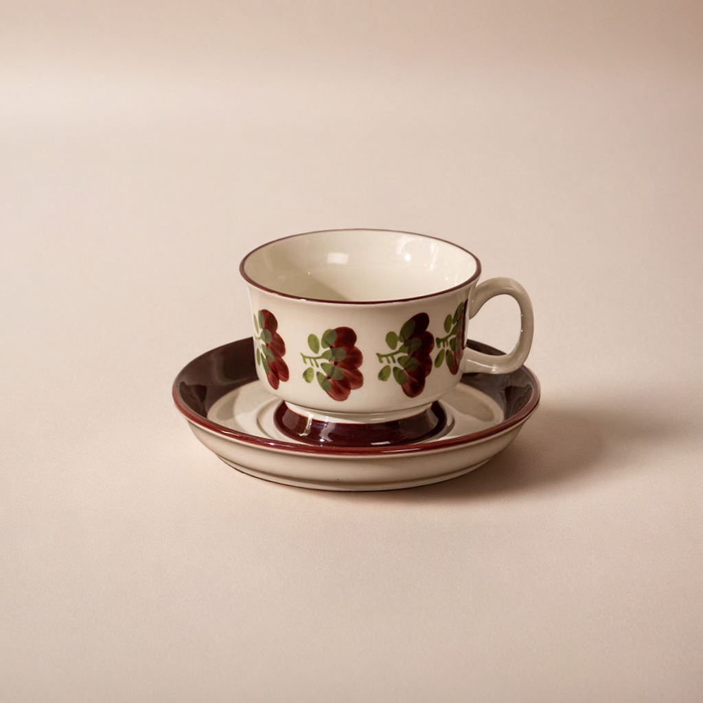 A ceramic tea cup with a hand-painted grapevine motif in deep burgundy and green on a cream base. Microwave safe.