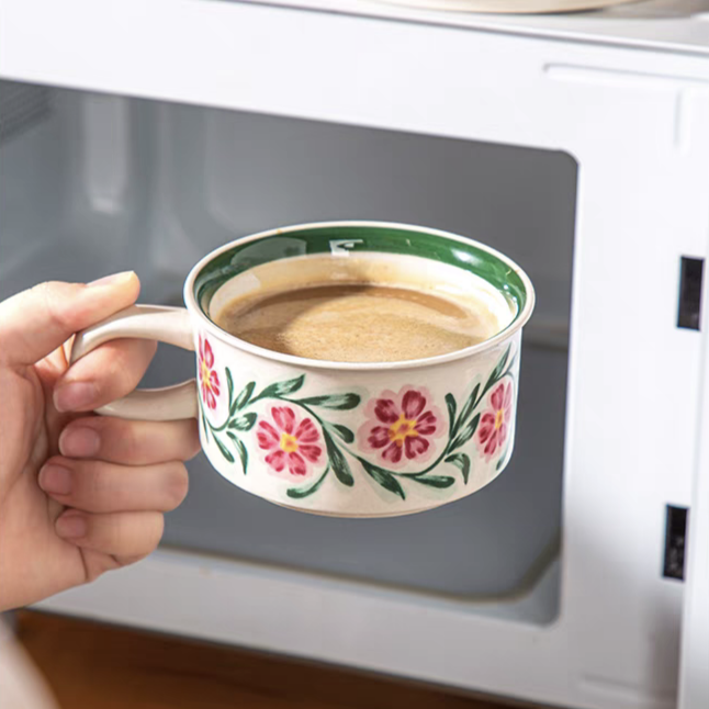 A latte-filled ceramic cup with hand-painted floral designs, ideal for adding elegance to your table. Microwave safe.