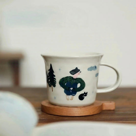 Aesthetic ceramic coffee mug featuring a whimsical hand-painted scene of a little girl in a green coat and a black cat surrounded by illustrated trees. This kawaii and cottagecore-inspired mug has a glossy finish and speckled glaze, ideal for cozy mornings and fans of forest-themed decor.