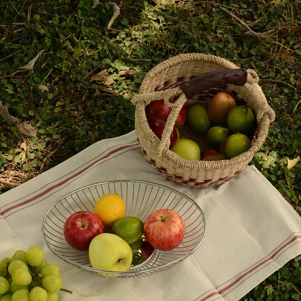 Hand-woven seaweed basket filled with fruits, sitting on a blanket, perfect for eco-conscious outdoor activities.