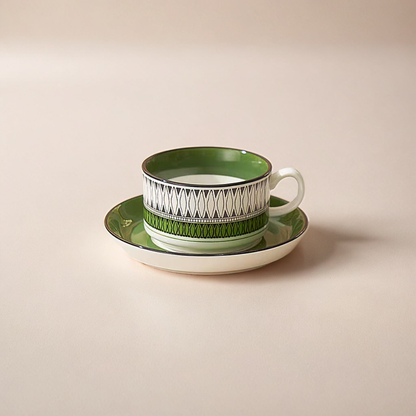 A boho-style ceramic mug with bold green patterns and a saucer for coffee or tea.