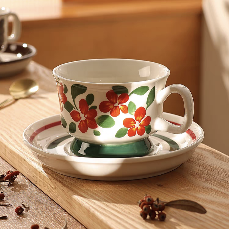 A ceramic coffee cup featuring hand-painted red flowers with green leaves, showcasing its minimalist floral design and smooth finish.