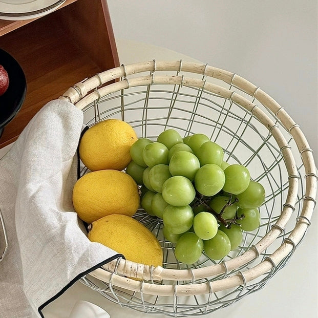 Round woven metal wire storage basket filled with fresh fruits, showcasing Scandinavian minimalism and natural rattan design.