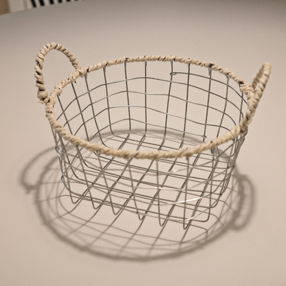 Full view of the round woven metal wire basket with handles, showcasing its size and decorative features suitable for various storage needs.