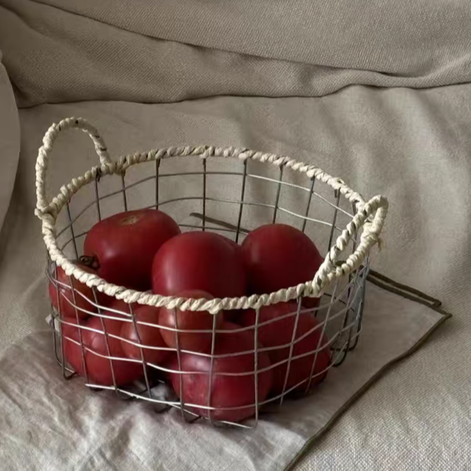 Stylish round woven metal wire storage basket holding a variety of fruits and vegetables, perfect for a natural-inspired kitchen decor.