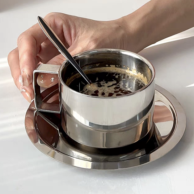 Minimalist stainless steel coffee cup with matching tray and spoon, designed for a stylish kitchen or living room setting.