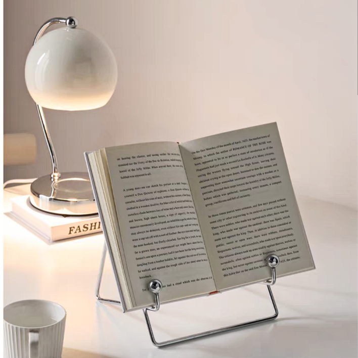 Stylish stainless steel book stand with a sleek, minimalist design, displayed with a book.