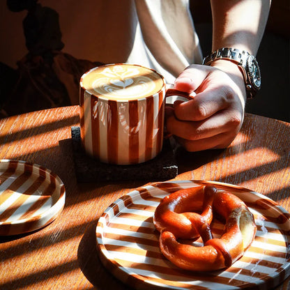 Durable and versatile ceramic cup and matching plates with burnt orange stripes, perfect for hot beverages, desserts, and appetizers in a retro home.