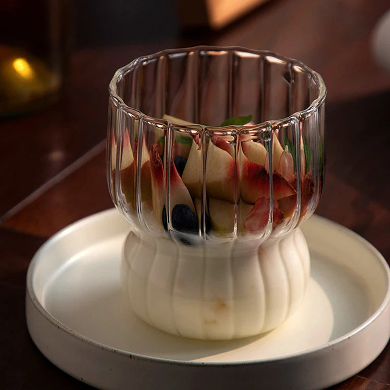 A ribbed glass cup filled with yogurt and fruit toppings, highlighting its elegant wavy rim and smooth round base.