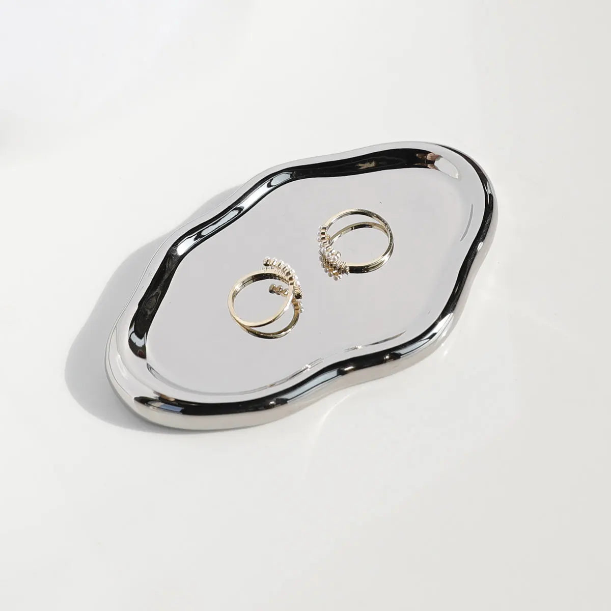 Silvery oval-shaped metal decorative tray, showcasing a modern design and holding rings and necklaces, ideal for jewellery organization.