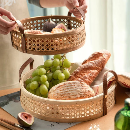 Handmade rattan storage trays in natural and walnut wood colors, filled with fruits and bread, featuring leather handles for easy carrying and available in multiple sizes.