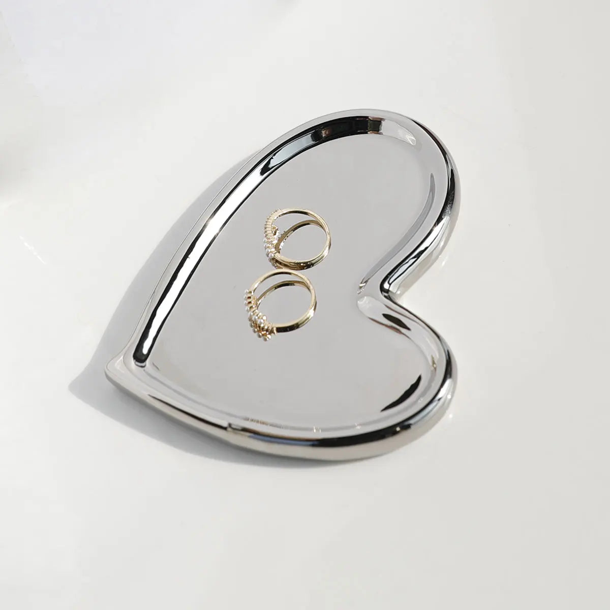 Silvery heart-shaped metal decorative tray, displaying bracelets and earrings, perfect for elegant jewellery storage.