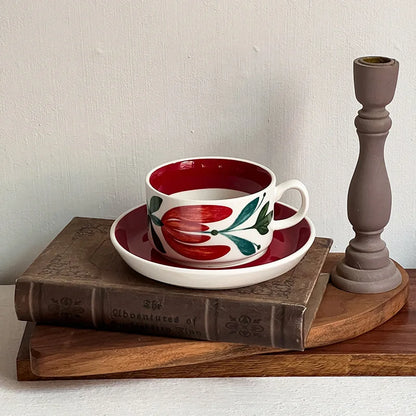 A bold red ceramic cup with floral motifs, paired with a saucer for stylish table settings.