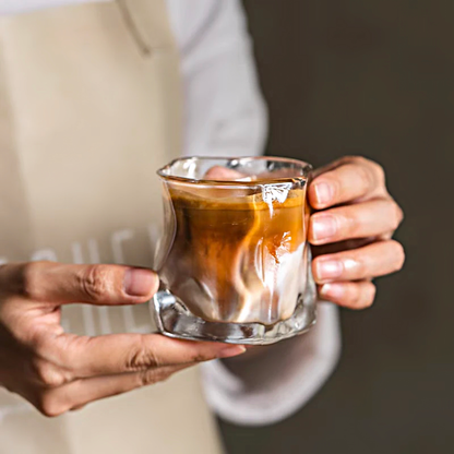 Dirty coffee served in a minimalist glass cup, emphasizing its sleek, wavy design and Scandinavian style.