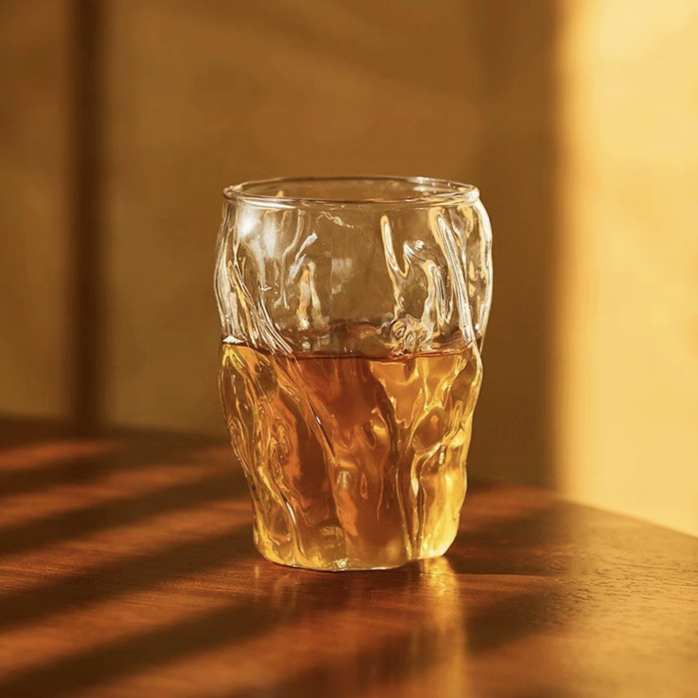 A minimalist glass cup filled with tea, featuring a glacier pattern and artisan craftsmanship, perfect for daily use.