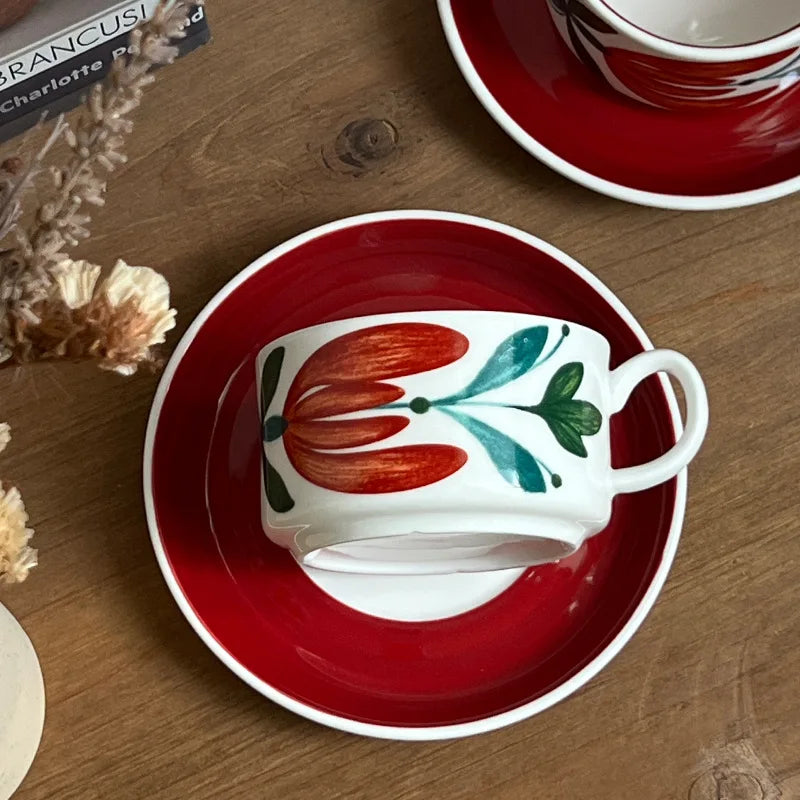 A red ceramic mug with intricate floral patterns, paired with a saucer for elegant table settings.