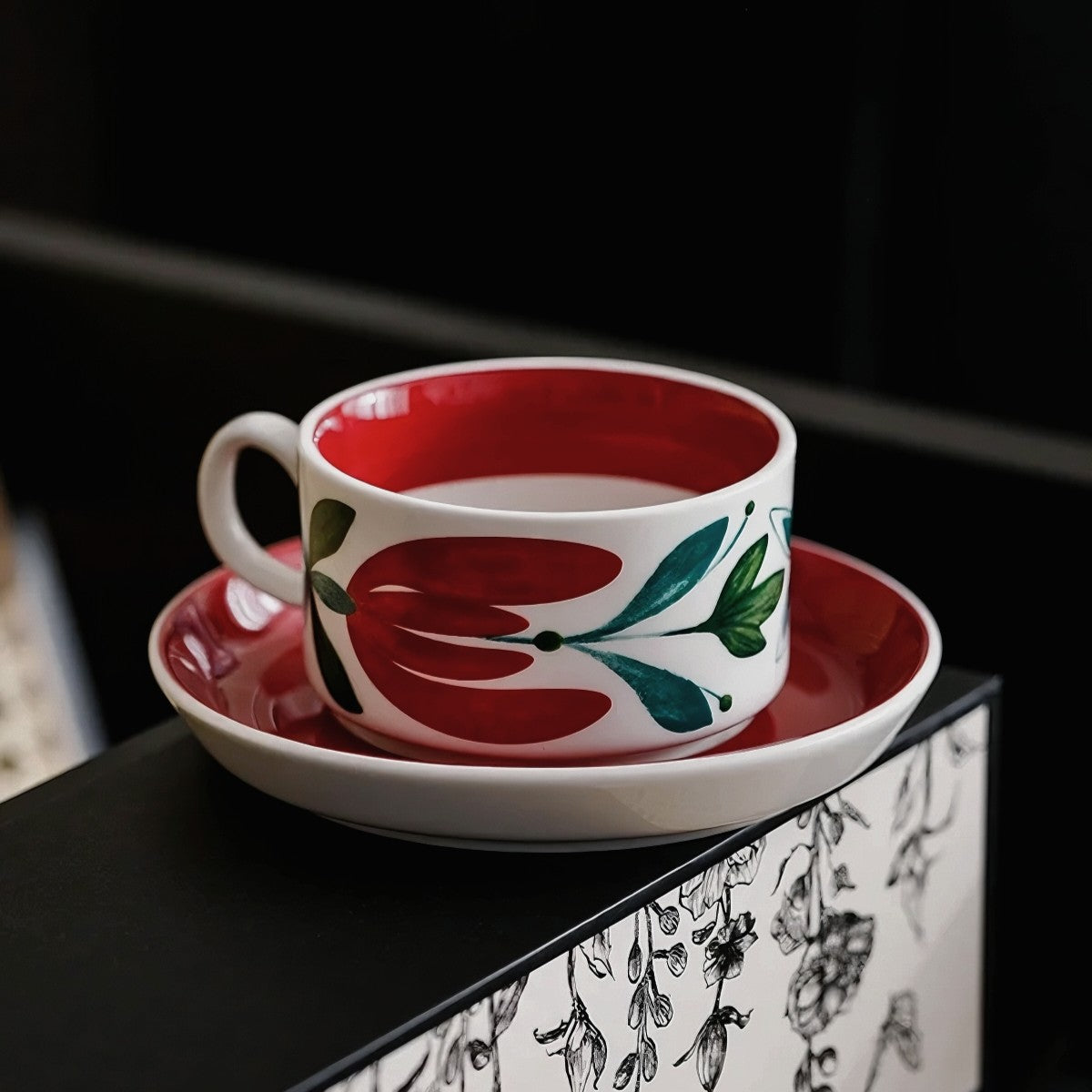 A bold red ceramic mug with Scandinavian-inspired floral patterns, paired with a saucer for tea or coffee.