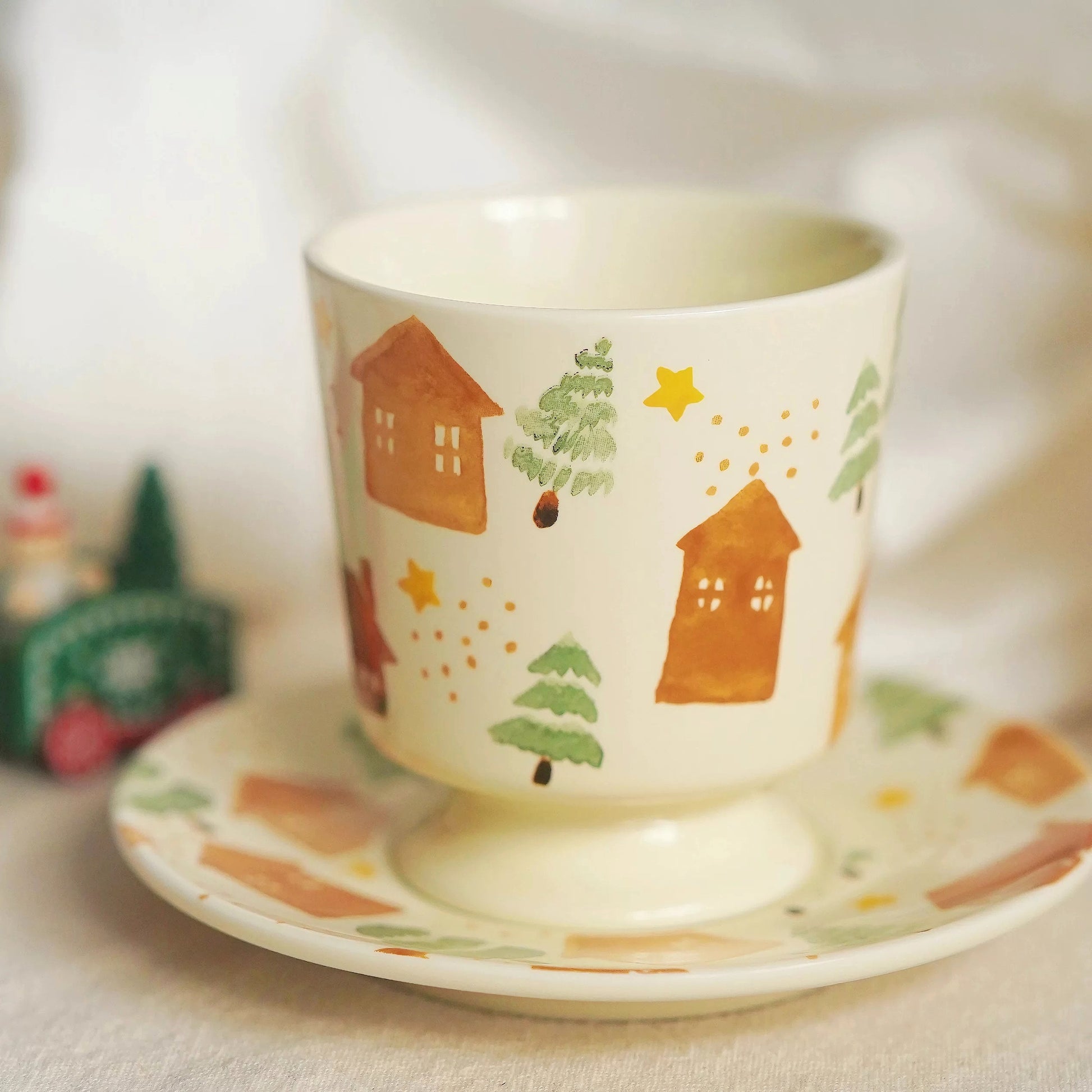 Aesthetic hand-painted ceramic coffee cup and saucer featuring snowy village illustration and Scandinavian folk art design.