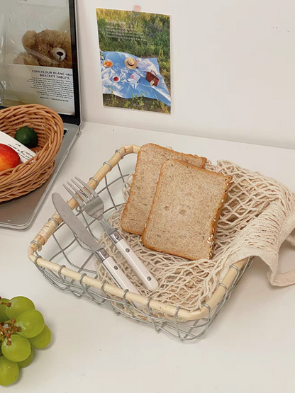 Eco-friendly square storage basket holding breads and forks, blending metal and rattan for a stylish and functional kitchen solution.