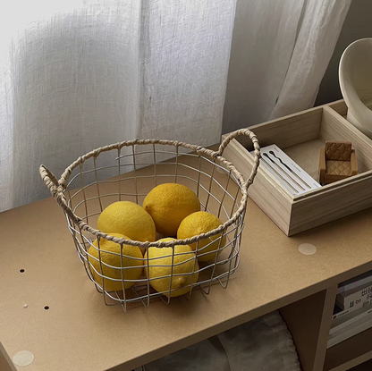 Round woven metal wire storage basket with handles filled with fresh lemons, showcasing Scandinavian minimalism and aesthetic design.