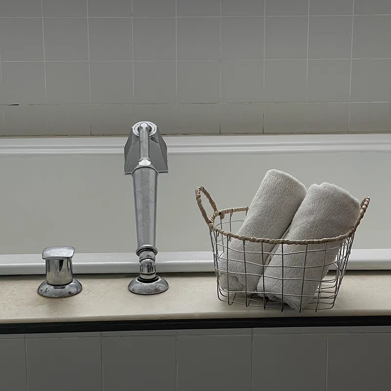 Round woven metal wire storage basket with handles used to store rolled towels, adding a touch of Scandinavian minimalism to the bathroom.