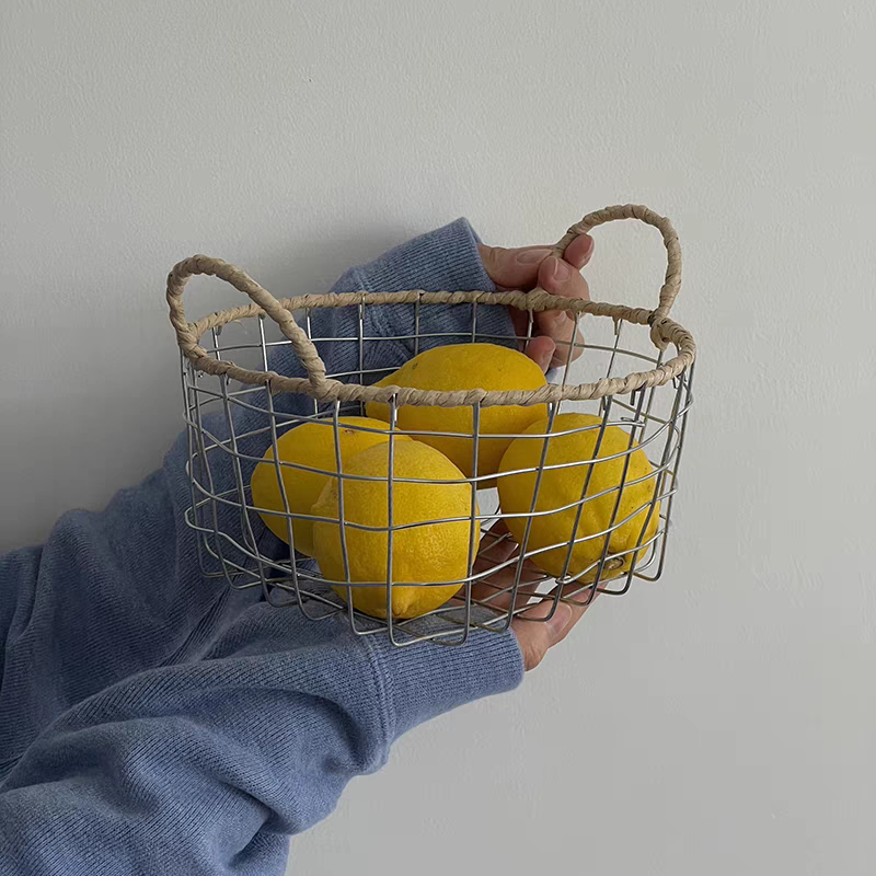 Aesthetic round woven metal wire storage basket with handles, holding an assortment of fruits, ideal for kitchen storage ideas.